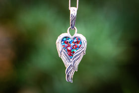 Photograph depicts the angel Wing Heart Pendant hanging from a chain. The pendant contains red and turquoise crushed opal.  Necklace for ash, necklace for cremation ash, necklace for cremains, angel necklace