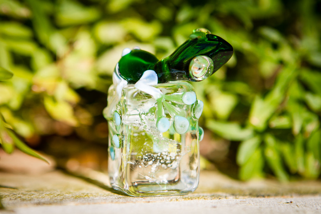 Close up of green glass frog on a transparent block with turquoise beads, showcasing cremation ash infusion