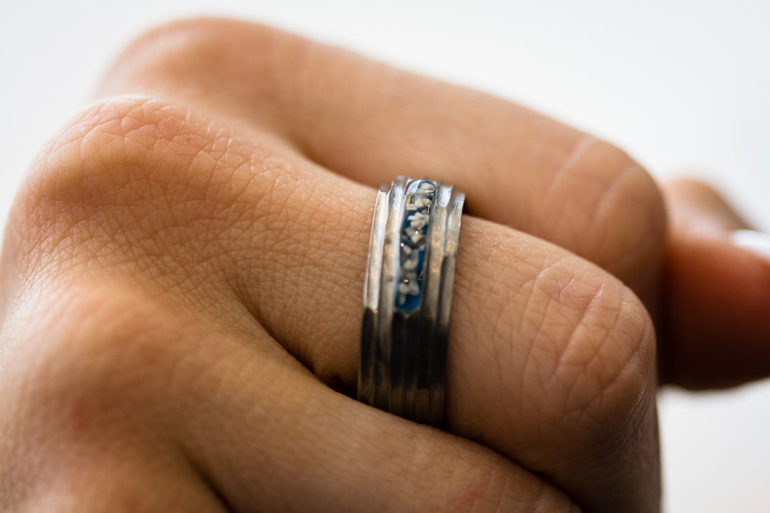 Close-up of a titanium ring on a finger featuring a blue inlay and crystal accents