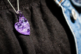 cremation heart pendant with cremation ash hanging in purple on cloth side view