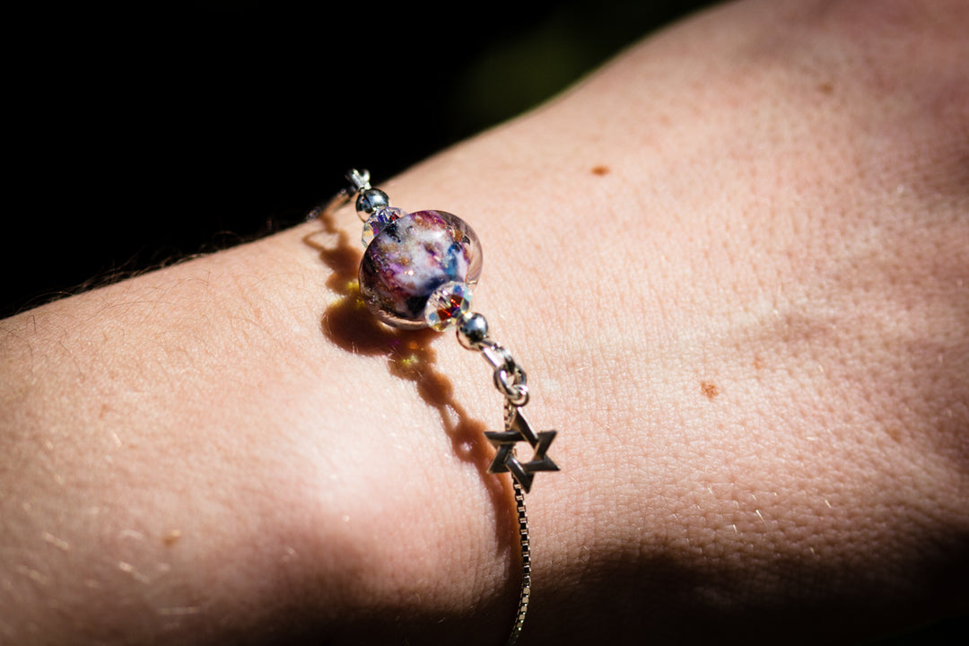 Wrist wearing a glass bead bolo bracelet with cremains and star charm on a silver chain