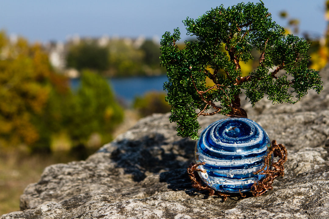 Ponderosa Tree of Life wire sculpture with a blue bubble twist orb memorial resting on a rock outdoors