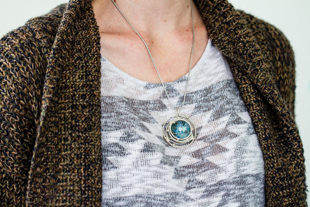 Person wearing the galaxy pendant on a silver chain over a patterned knit top