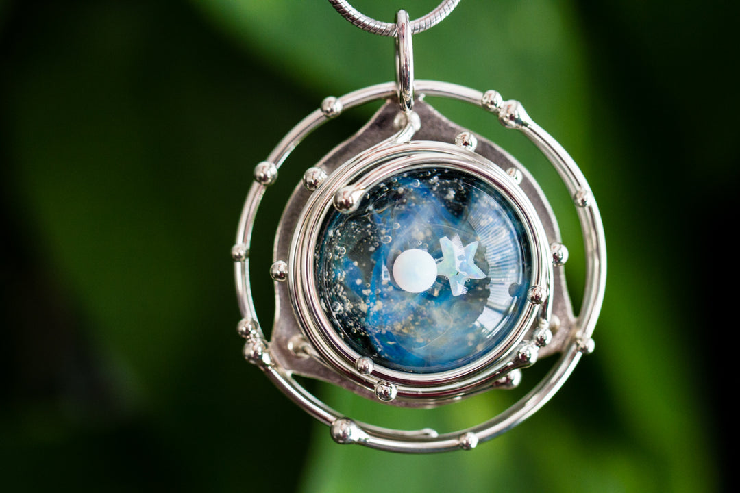 Caged glass galaxy pendant with two opal accents inside a circular frame