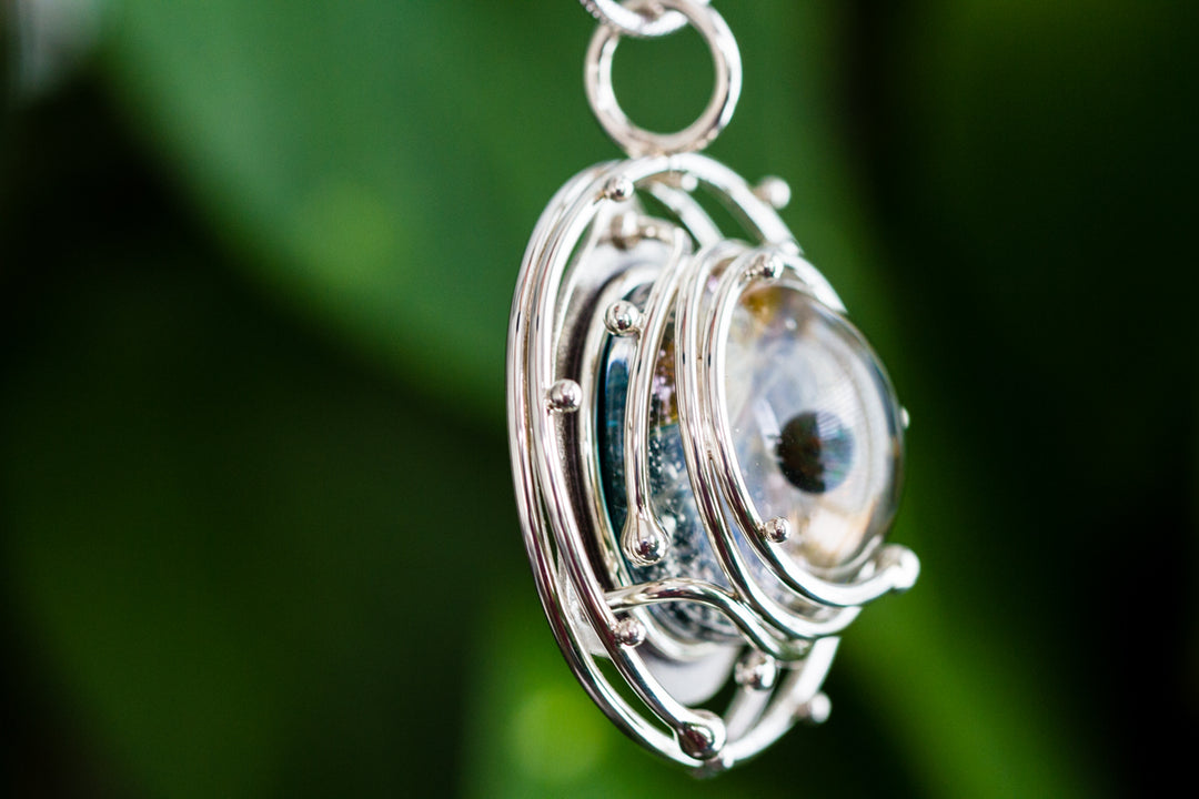 Close-up of a caged glass galaxy pendant with opal in a silver orbital cage