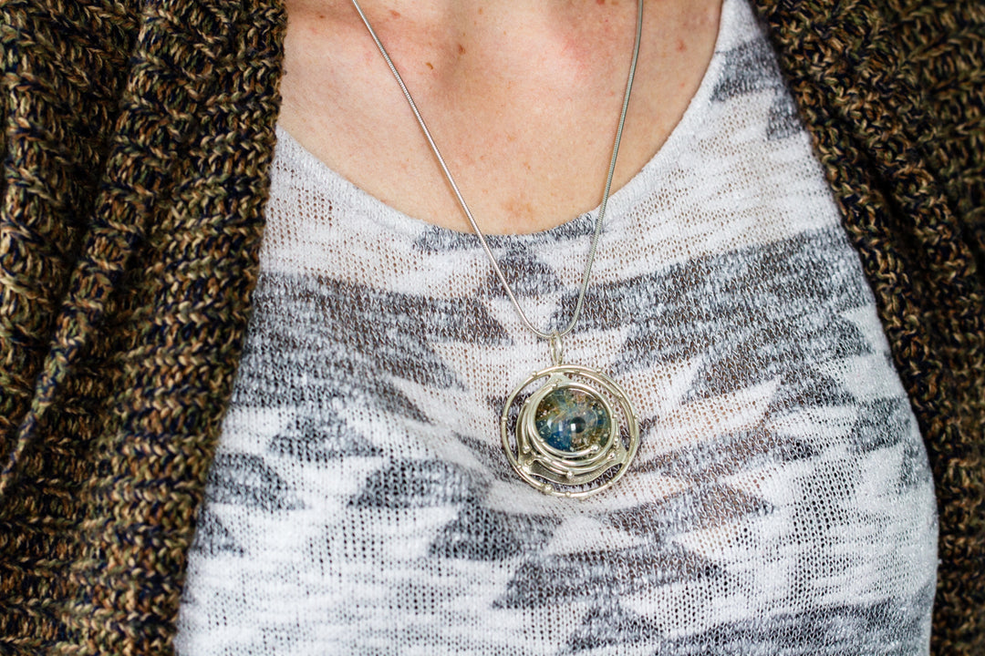 Caged glass galaxy pendant with opal on a silver chain worn on the chest