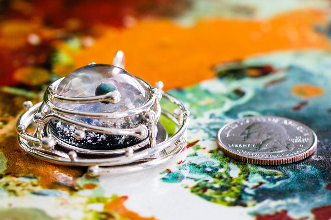 Silver circular caged pendant with a glass galaxy cabochon and opal, photographed against a pale background.
