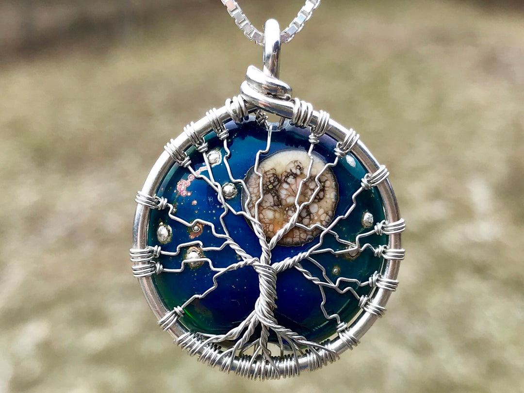 Moon and Stars Tree of Life pendant with cremains showing a silver wire tree against a blue glass circle with a central moon bead and tiny stars