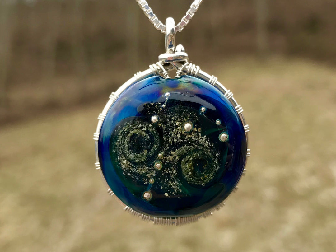 Moon and Stars Tree of Life pendant with cremains set in a deep blue glass disk with spiral galaxy patterns and a silver wire tree wrapped around the edge
