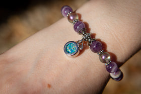 Main listing photo contains a wrist wearing the Amethyst Healing Bracelet. The dainty circle charm rests atop the hand, facing the viewer. The charm contains light blue and turquoise opal. Amethyst bracelet, sterling silver bracelet, bracelet for cremation ash, remembrance bracelet