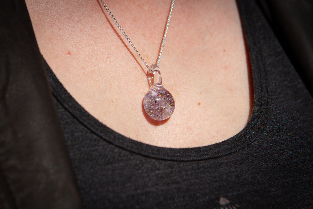 Clear round glass pendant with lavender pink flecks containing cremation ashes on a silver chain