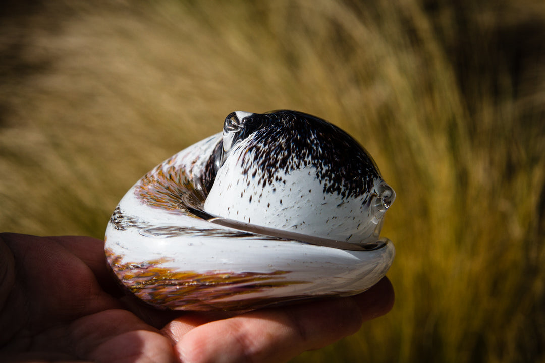 Handheld calico glass cat paperweight showing a curved base and cremains beneath clear glass.