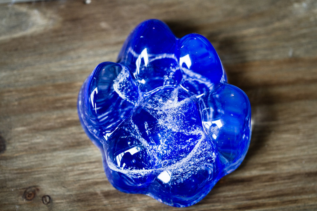 Cobalt blue Memorial Glass Paw Print with ash embedded on a wooden surface