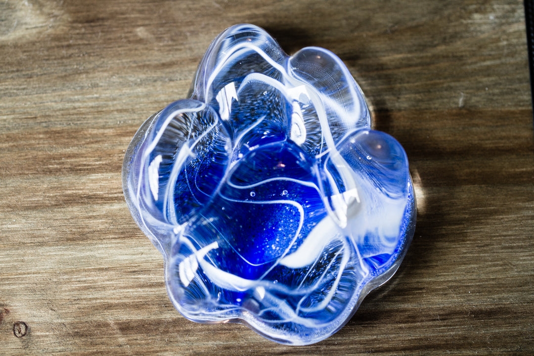 Clear Memorial Glass Paw Print with white streaks swirling through the paw on a wooden surface