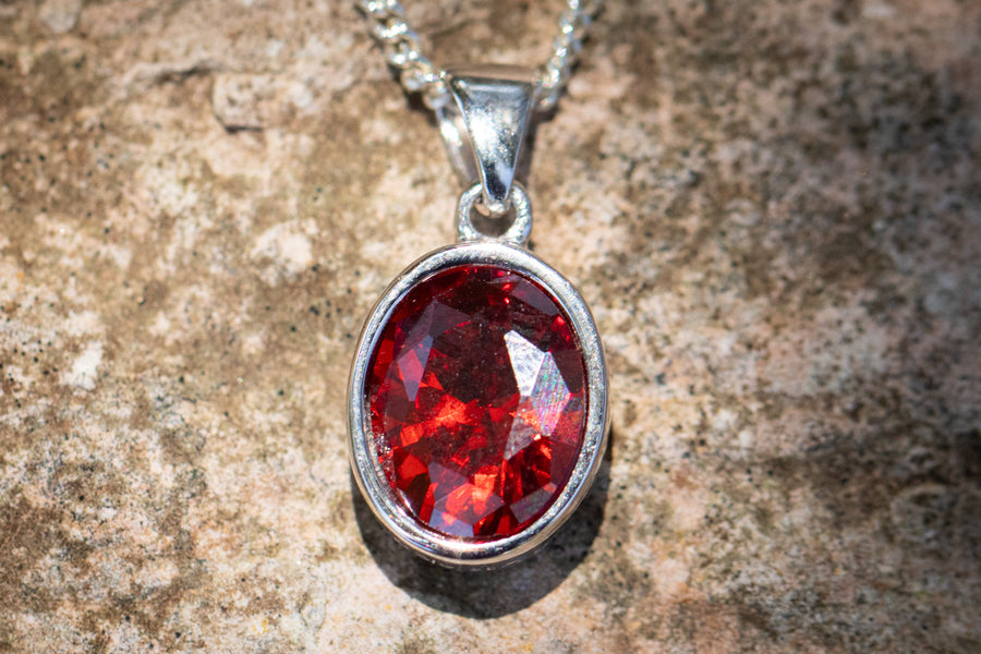 Red crystal drop memorial pendant with silver setting on a chain designed to hold cremation ash.