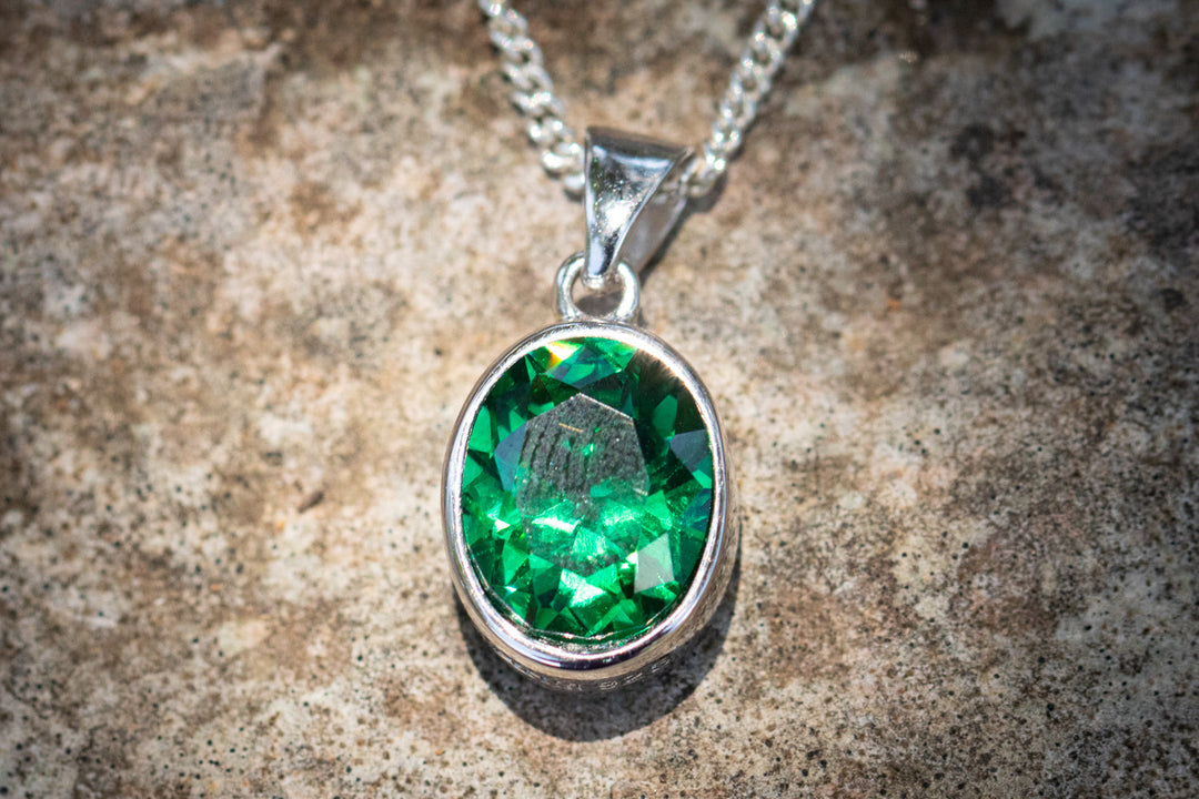 Green crystal drop memorial pendant with silver setting on a chain designed to hold cremation ash.
