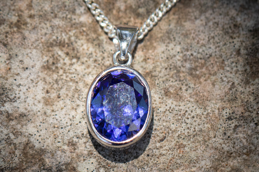Oval blue purple crystal memorial pendant in a silver bezel with chain against a stone background