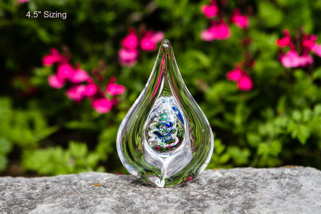 Teardrop glass flame drop with cremains and a colorful inner swirl photographed outdoors.