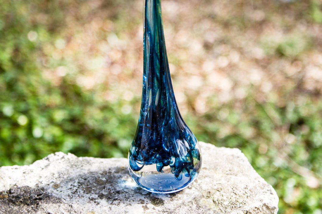 Curly blue glass angel drop infused with cremation ash on a 3 inch light stand outdoors