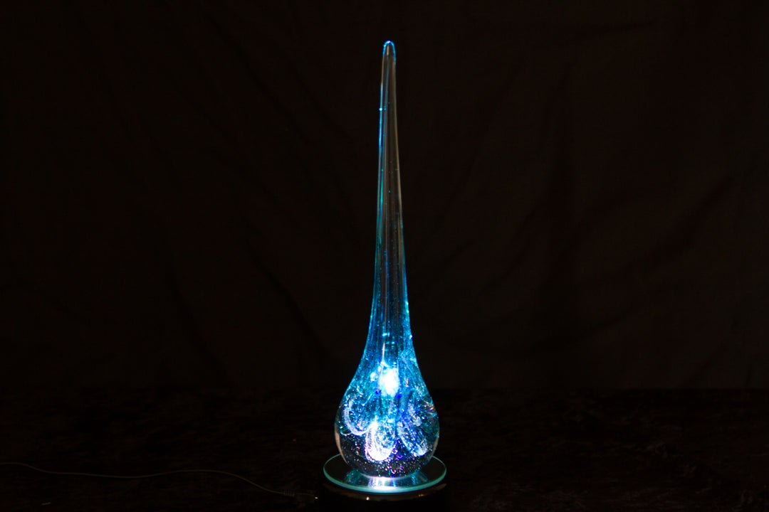 Tall blue illuminated glass angel drop infused with cremation ash, glowing from within on a circular base.