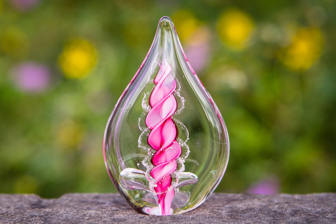 Clear glass memorial flame with a pink spiral interior containing cremation ashes