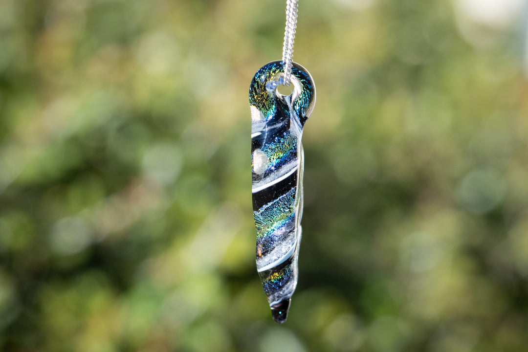 Slim elongated dichroic ripple pendant with cremation ashes and vivid rainbow swirls on a chain
