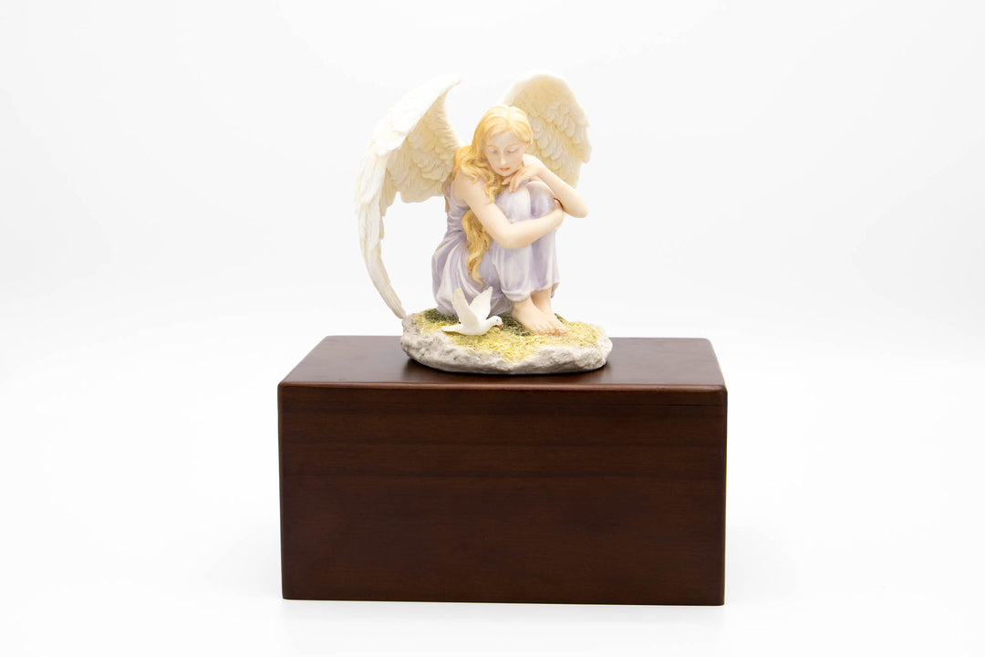 Sitting angel with a dove figurine on a rocky base atop a dark wooden urn topper