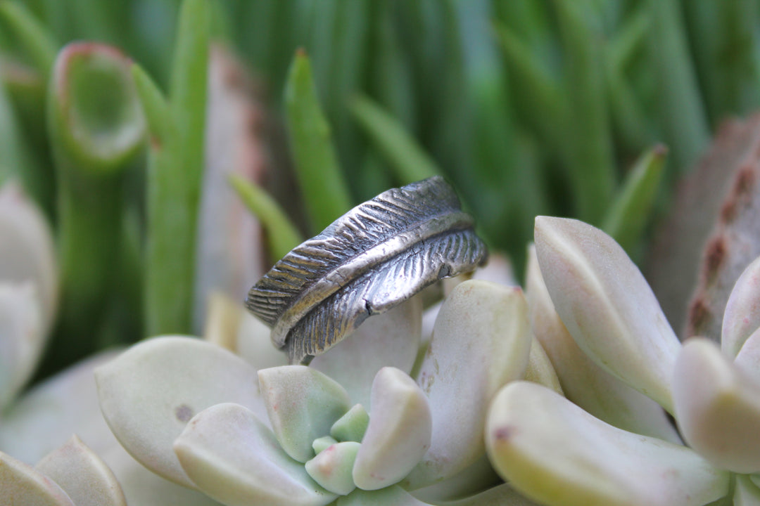 Silver feather ring with antique finish displayed on a succulent plant, highlighting the feather texture