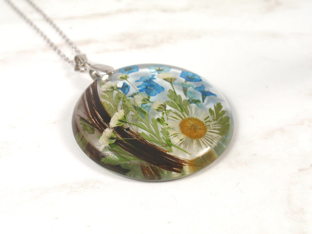 Round crystal resin pendant filled with blue blossoms and a white daisy inside.