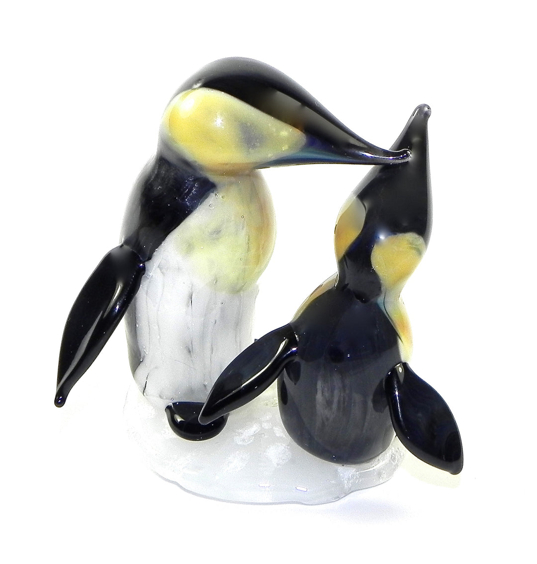 Two glass penguin figurines infused with cremation ashes on a white base facing each other