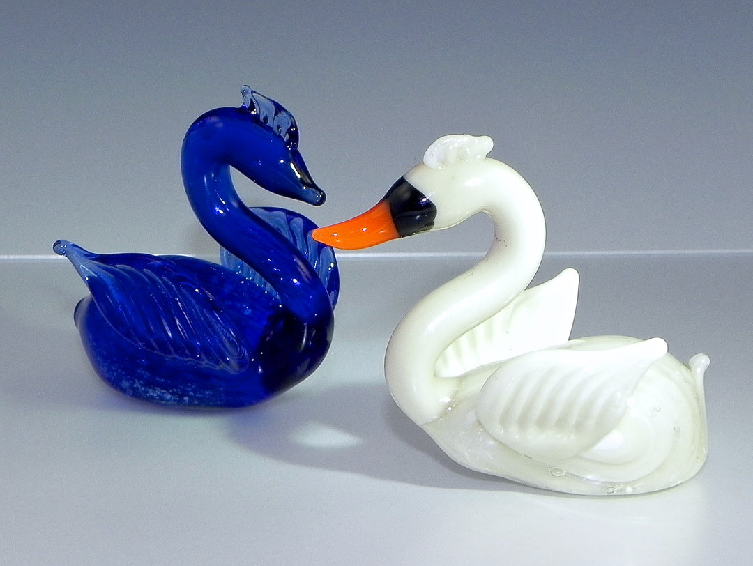 Two glass swans facing each other, one cobalt blue and one white with an orange beak.