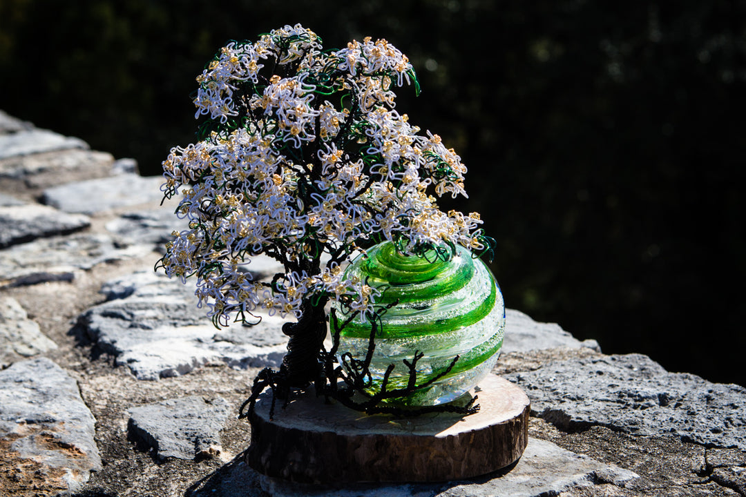 White Dogwood Tree of Life sculpture with a green swirled orb on a wooden base outdoors