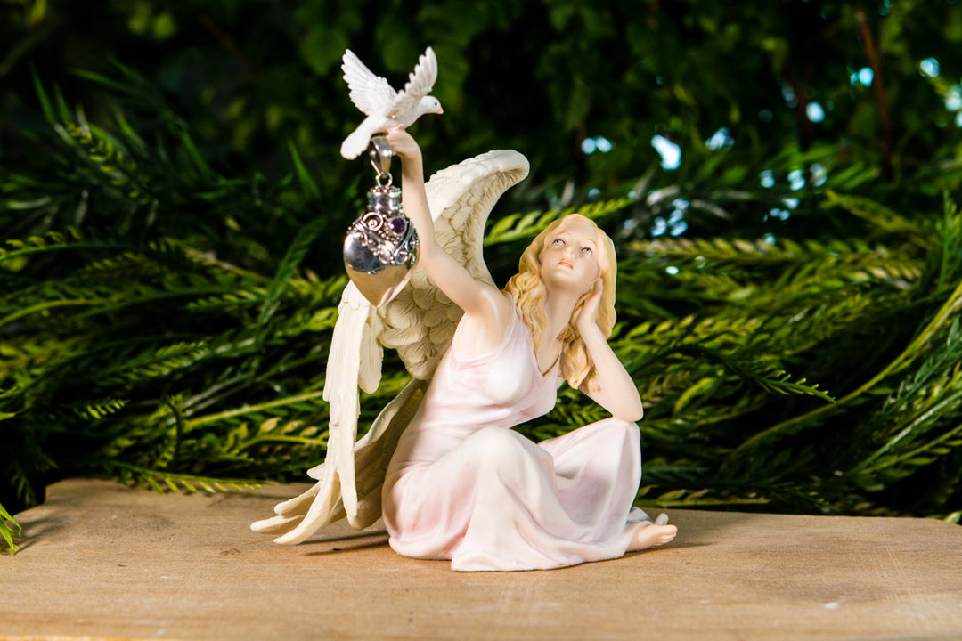Angel keepsake figurine holding a silver heart pendant urn and a dove perched nearby