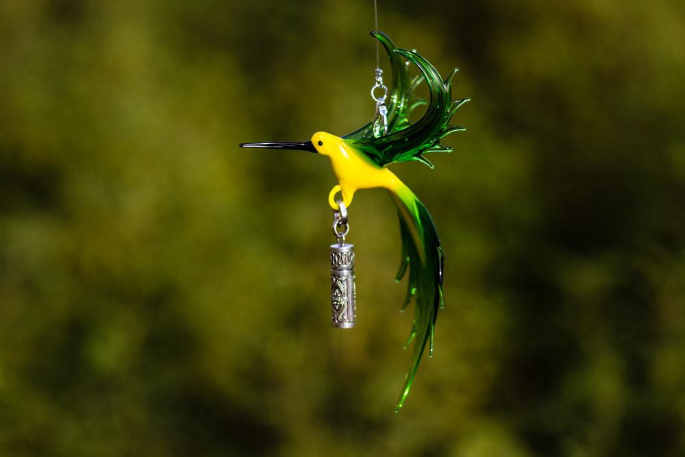 Bee eater glass bird with a sterling silver keepsake urn pendant against a soft green background.