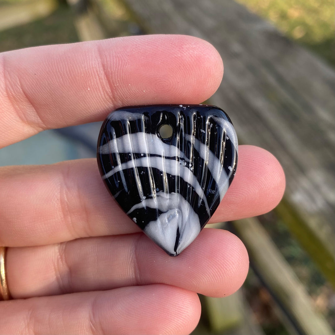 Ash infused borosilicate glass guitar pick with black base and white swirls held between fingers