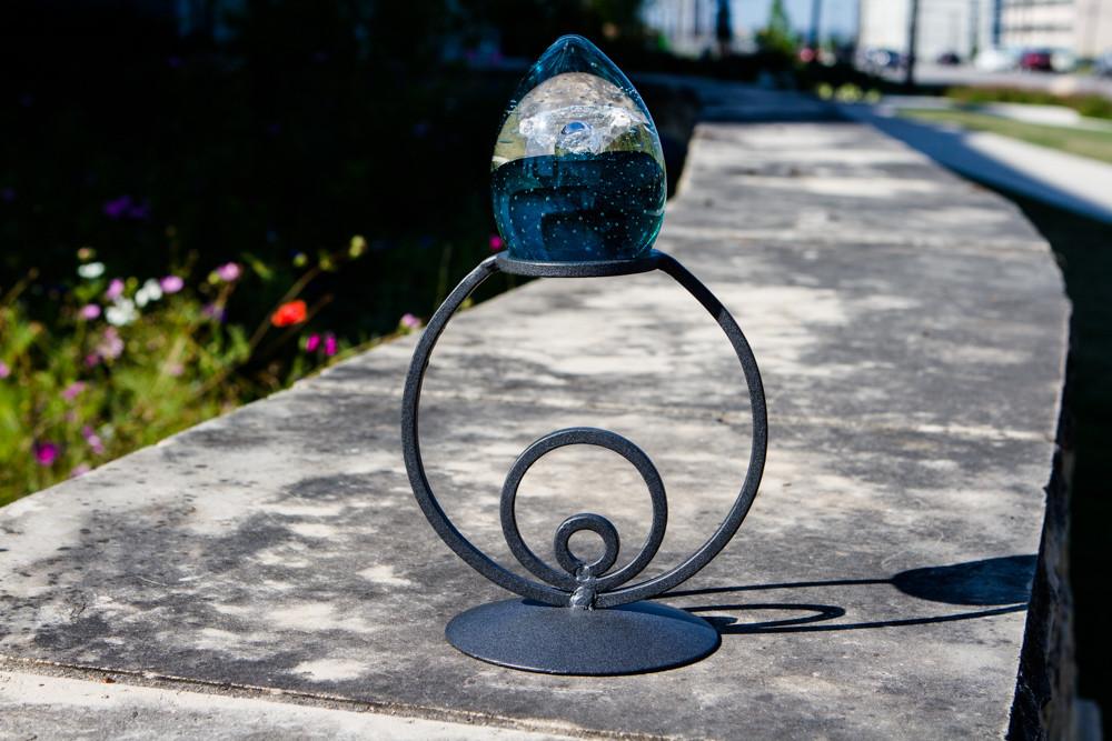 Black wrought iron circle stand with a blue glass orb perched on a stone ledge outdoors