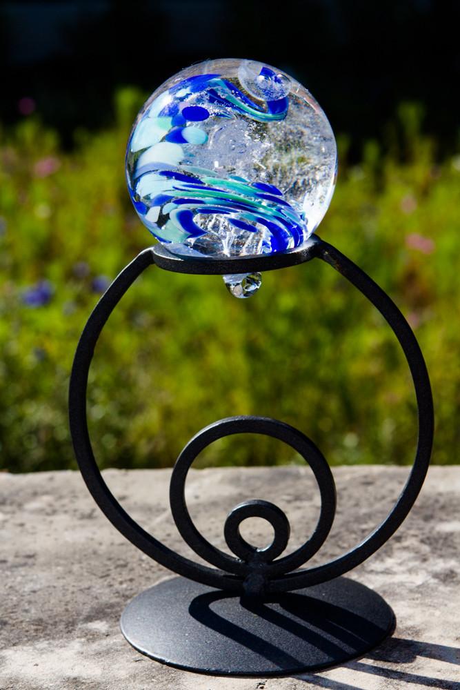 Black wrought iron circle stand with a glass orb perched on top in an outdoor setting.