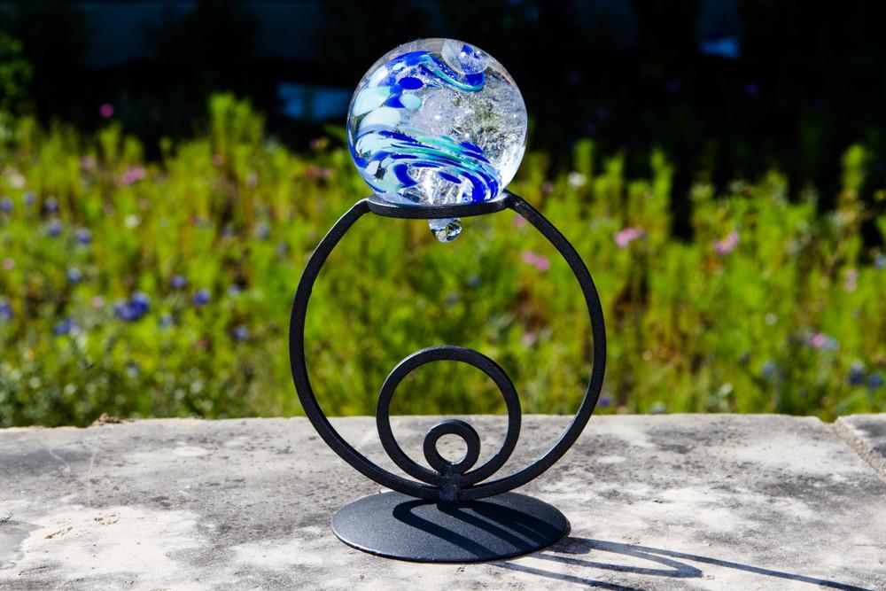 Close up of glass orb resting on a black wrought iron circle stand.