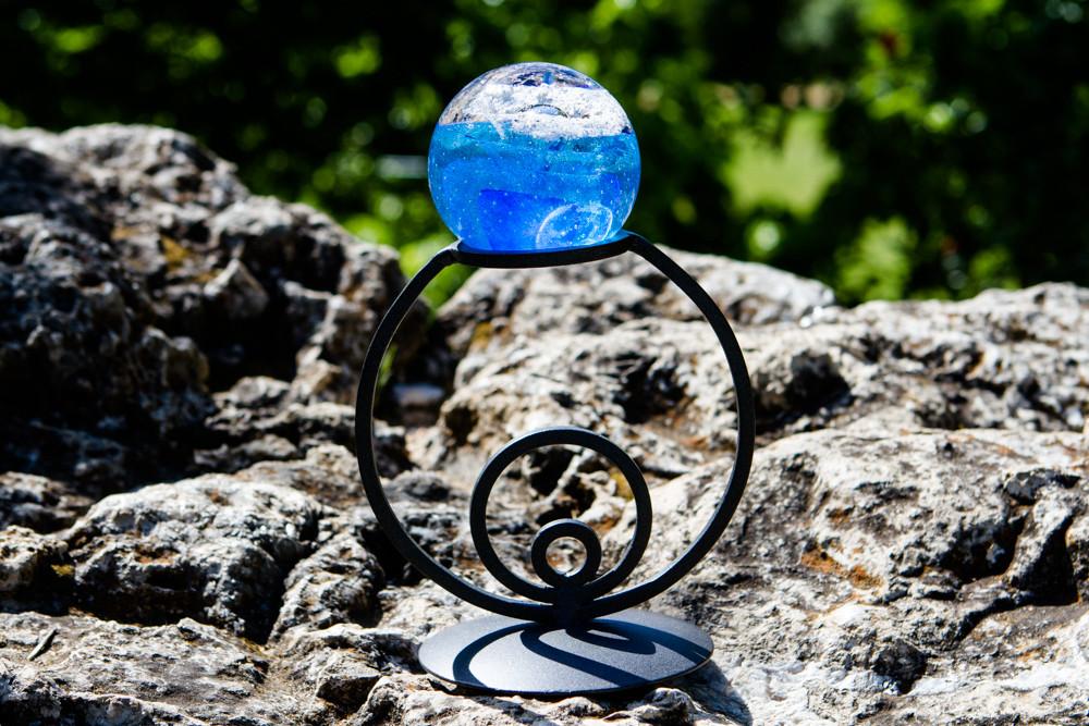 Black wrought iron circle stand with a blue glass orb resting on top outdoors