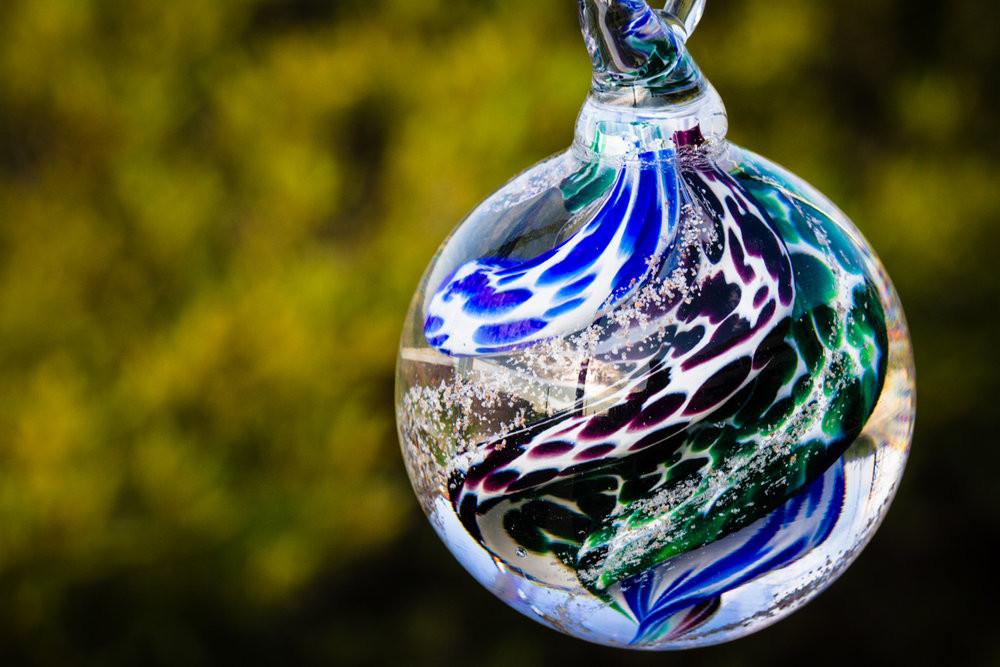 Swirled blue green cat eye cremation orb with speckled pattern hanging outdoors