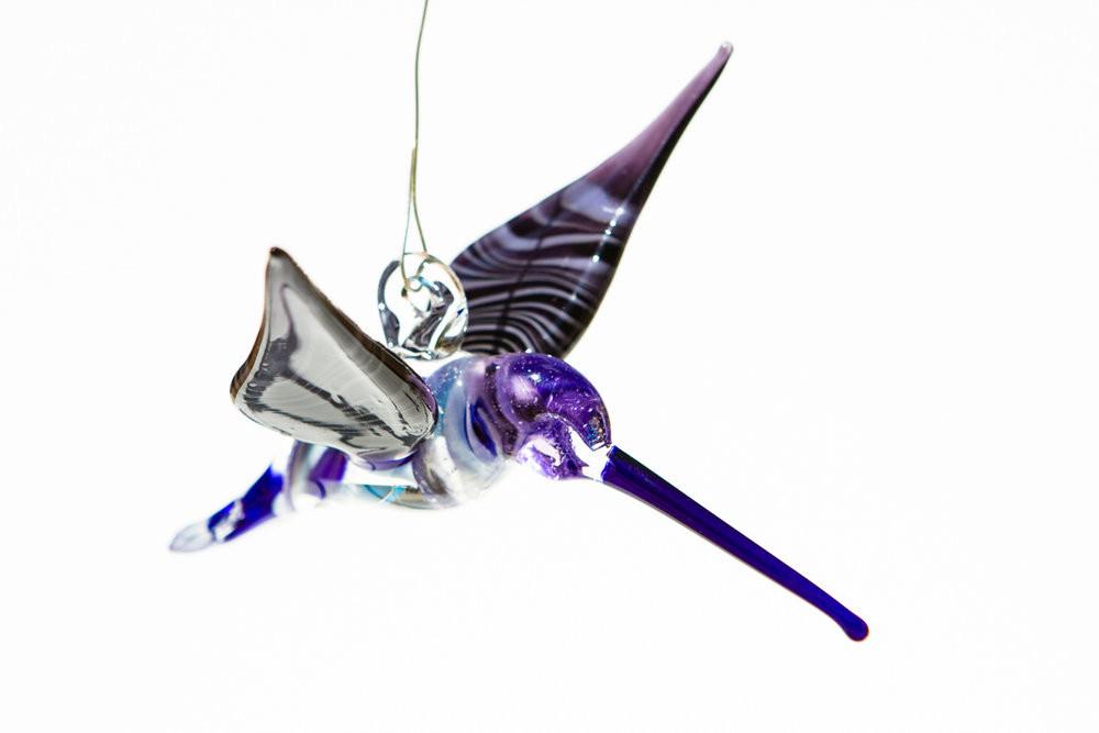 Side view of a blue and purple glass hummingbird infused with ashes, with a long purple beak and top hanging hook.