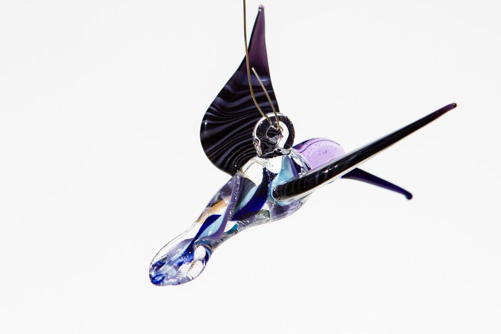 Hanging glass hummingbird with cremation ashes, blue and purple swirls, shown from a side view with a top hook.