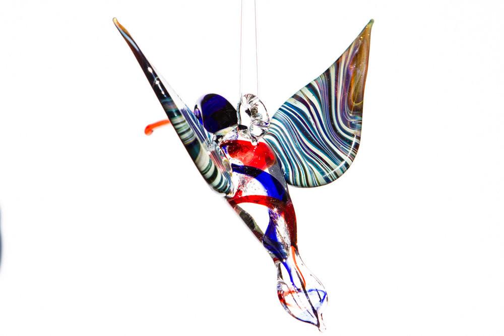 Blue and red cremation ashes swirl through a glass hummingbird with a hanging hook.