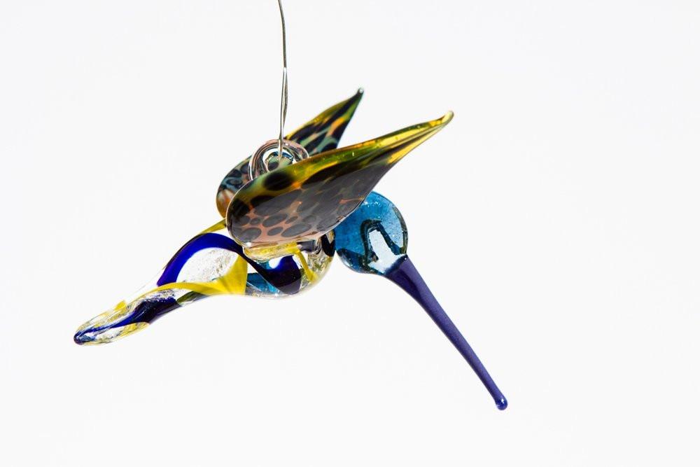 Side view of a blue and yellow glass hummingbird infused with ashes and a hanging hook.