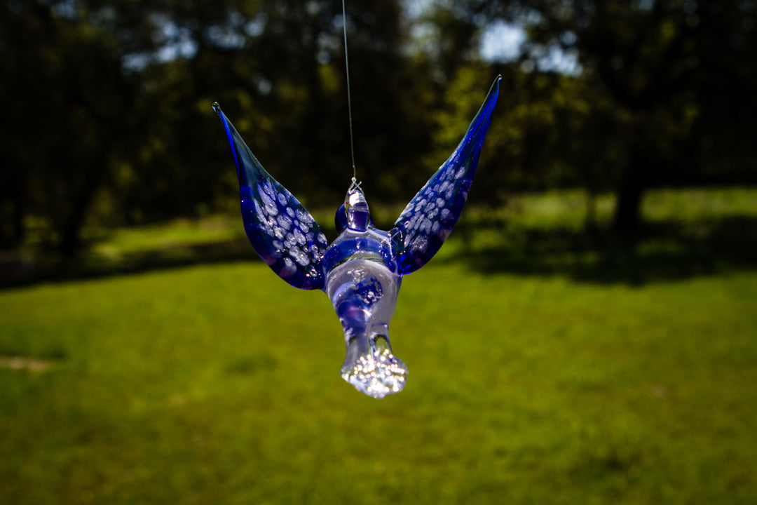 Blue glass hummingbird ornament infused with cremation ashes, hanging by a string