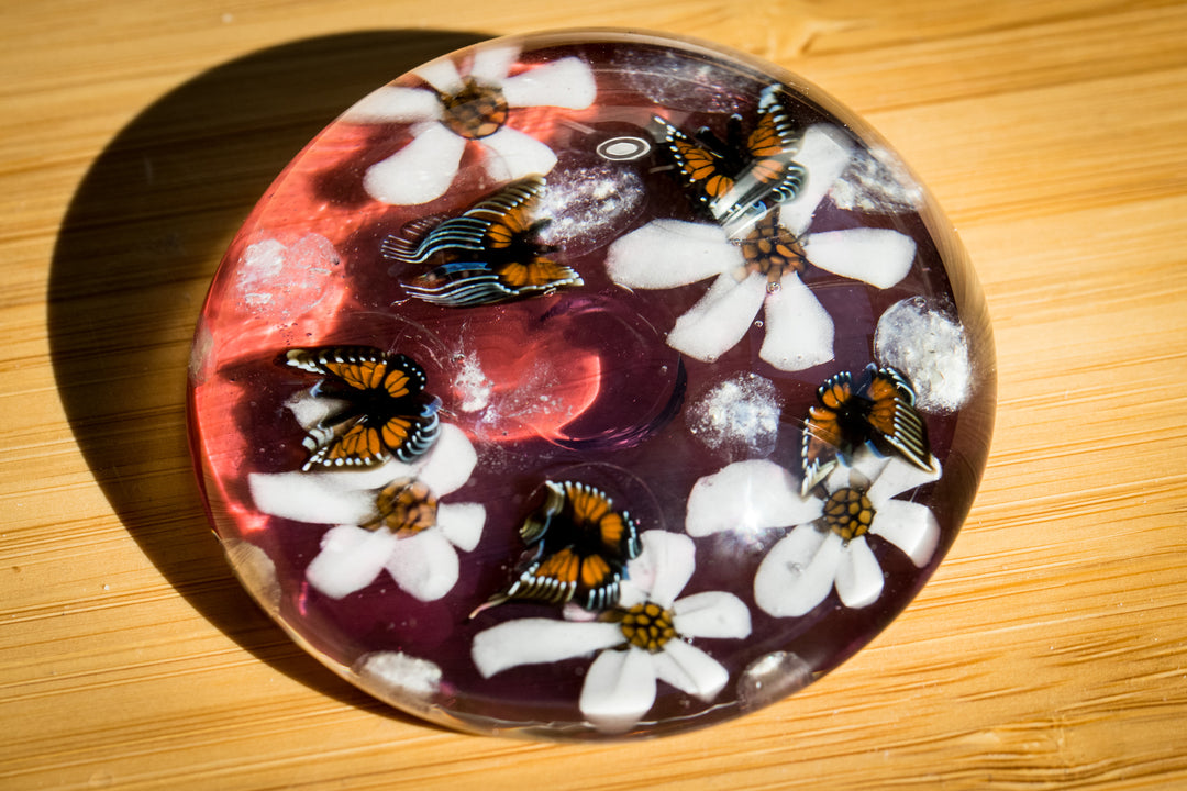 Round glass paperweight with butterfly motifs and white flowers on a purple background