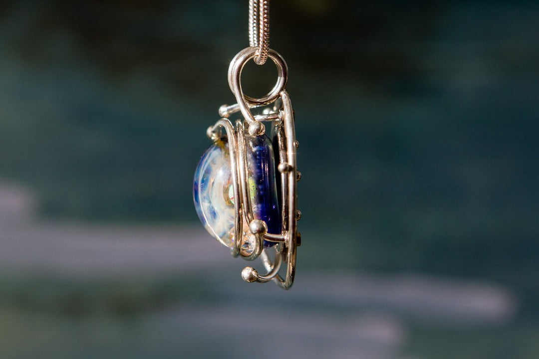 Glass cabochon with galaxy design encased in a silver cage pendant on a chain.