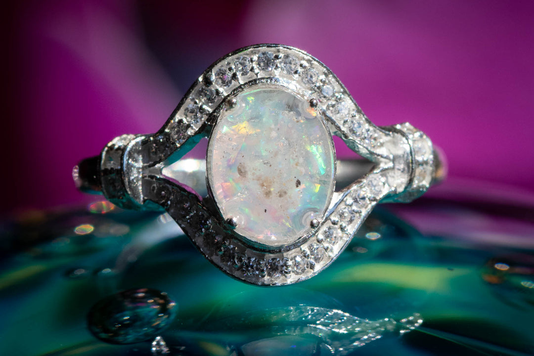 Oval Eye Ring with white opal sitting atop a glass surface. Sterling Silver Ring, Sterling Silver Ring with Zircon, Sterling Silver Ring for Ash, Silver Ring for Cremains, Jewelry for Cremation Ash, Remembrance Jewelry, Silver Remembrance Jewelry