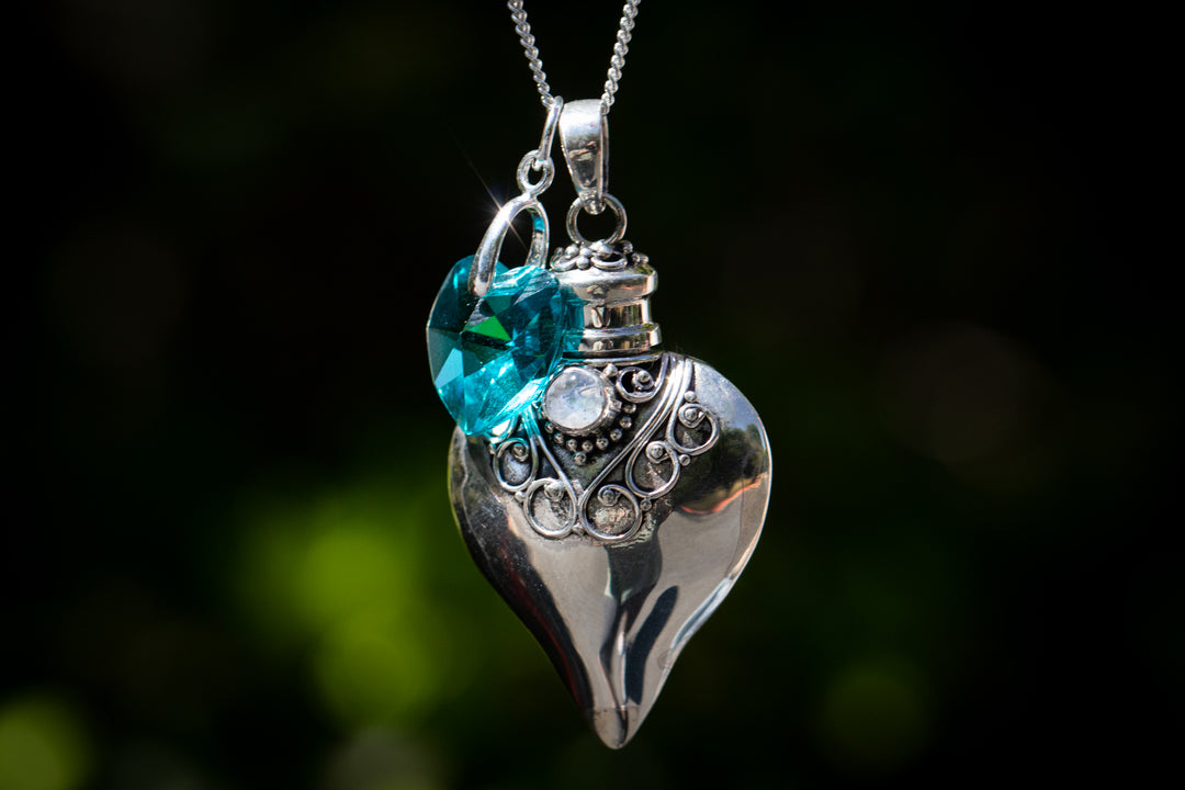 Silver heart cremation pendant with a teal crystal and ornate detailing on a chain