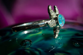 Side view of the sterling silver Bedazzled Starfish Ring, with light blue opal, sitting atop a glass surface. Sterling Silver Ring for Ash, Sterling Silver and Zircon Ring, Ring for Cremation Ash, Silver Remembrance Jewelry, Jewelry for Ash